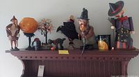 Full lot of vintage Halloween decorations including figures, tree, boot, cat, and mug arranged on a wooden shelf