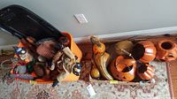 Wide view of plastic bin filled with fabric stuffed decorations, beside a box holding various pumpkin and gourd decorations placed on the floor.