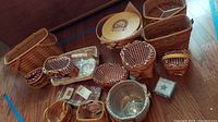 Photo shows assortment of various Longaberger baskets including rectangular, round, oval and smaller baskets with cloth and plastic inserts alongside a few unopened package inserts.