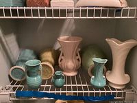 Eight McCoy and USA pottery vases arranged on a white wire shelf showing variety of shapes and colors.