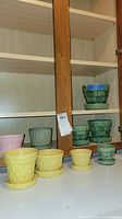Photo showing yellow, green, and pink McCoy planters arranged on a surface, exhibiting textured and patterned ceramic designs, all with matching saucers.