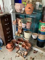 Full view of metal rack holding various terracotta and ceramic planters and pots. Includes smaller pots, some with wear and chips.