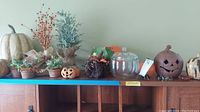 Long view of the shelf showing two large pumpkins, small ceramic pumpkin with face, glass pumpkin, spider, berry branches, and several small faux plant pots.