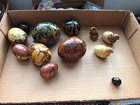 Overall photo showing the group of 11 ceramic eggs and chicks with various hand-painted designs and glazes inside a cardboard box.