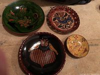Four colorful redware pottery bowls arranged on a surface showing various folk art designs