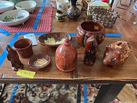 Photo showing eight pieces including animal banks, bowls, and covered pottery piece on a wooden table.