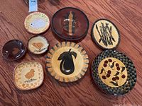 Eight redware plates arranged on wood surface showing various fruit, vegetable, chick and bunny folk-art designs.