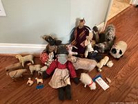 Overall assortment of handcrafted sheep figurines and plush dolls displayed on hardwood floor with a wall backdrop.