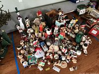 Wide view showing the full assortment of snowman themed decorations on the floor including figurines, candles, Pez dispensers, plush, and wooden items.