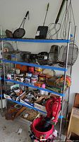 Full frontal view of stainless steel shelf containing various kitchen utensils, food tins, jars, tools, and a handheld vacuum cleaner.