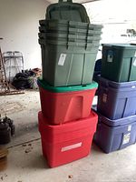 Stack of plastic storage bins showing olive green bins on top of red bins with green lids. Some bins have labels and scuff marks, bins are used and need cleaning.