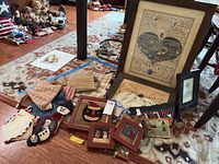 Wide view showing all items including framed textile art, quilt squares, crocheted pumpkin, linens and small framed prints on a rug.