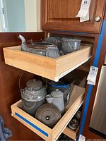 Photo showing two kitchen drawers with vintage graniteware items including kettles, canister, perforated bucket, colander, and measuring cup.