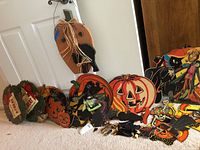 Photo showing an assortment of vintage cardboard Halloween decorations including pumpkins, witch, skeleton, scarecrow, with visible signs of wear including tears and separated pieces.