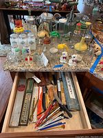 Overview of various kitchen gadgets on a granite countertop and inside drawer below showing cutlery, thermometer in box and drink stirrers.