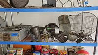 Metal kitchen items arranged on a wire shelf including a large metal box, strainers, scoops and other vintage utensils showing wear