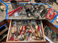 Assortment of vintage kitchen tools and utensils with red handles and metal components laid out on a granite countertop and in an open drawer.