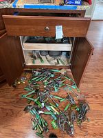 Photo of open wooden cabinet with kitchen utensils with green handles spilled on floor, showing quantity and condition of items.
