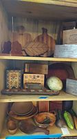 Wooden boxes, bowls, napkin holders, wooden cutting boards and vegetable-shaped wooden decor arranged on wood shelves.