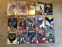 Photo showing 15 comic books laid out on brown carpet, including multiple Batman, Detective Comics, and Joker comics, some bagged.