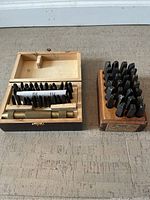 Two steel letter stamping kits with a variety of steel letters and stamps in a wooden box and a wooden block holder.