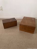 Two vintage wooden storage boxes on floor, smaller darker box on left, larger lighter box on right