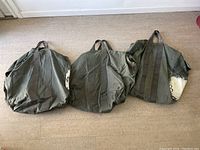 Three large military duffel bags placed on floor, showing size, color, and strap details.