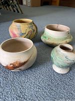 Four Native American Nemadji pottery pieces arranged on carpet floor showing marbled paint patterns in earth tones.