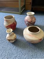 Four Nemadji pottery pieces grouped on carpet showing varied shapes and marbled swirl designs in earth tone colors.