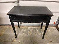 Full front view of the black wooden desk showing the single drawer and curved legs.