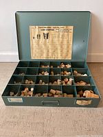 Closed green metal container with label on inside of lid showing cork stopper sizes and types.