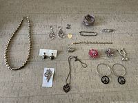 Full collection of costume jewelry items laid out on a beige cloth surface including necklaces, earrings, pins, bracelets, and rings