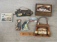 Full view of all 8 fishing decor items arranged on wall, showing various wood plaques, framed art, fish sculpture and wall rack.