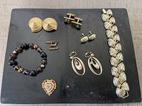 Full lot of goldtone costume jewelry on a flat surface. Includes multiple pairs of earrings, bracelets, pin, and a charm.
