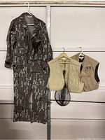 Camouflage coverall hanging next to two beige fishing vests, one with a fishing net attached.
