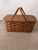 Side view of rectangular wicker picnic basket with wooden lid and two handles upright.