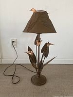 Full view of metal plant lamp with rust finish, showing base, stem, leaves, birds, and shade.
