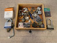 Overall view of the wooden tray containing assorted padlocks and keys, two larger padlocks outside the tray, and packaged lock hardware.