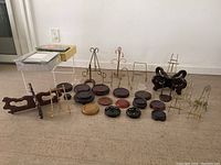 Photo displaying an assortment of wooden pedestals, metal easel stands in brass and metal finishes and various sizes, and wooden holders arranged on floor.
