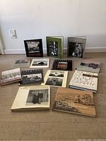 Wide view showing 13 photography books on floor arranged in several rows, mixture of hardcover and softcover.