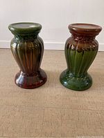 Side view of two ceramic planter pedestals showing ribbed design and two-tone glaze finish, green and brown.