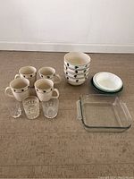 All items grouped together including mugs, bowls, glasses, and baking dish on floor.