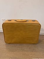Full front view of the vintage tan suitcase against a white wall and floor.