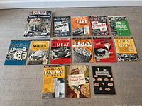 Wide view of all 14 vintage cookbooks and price guide arranged on floor, showing titles and cover art from 1940s era.