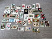 Overview of 38 assorted vintage postcards with floral and bird designs spread out on a grey fabric surface.