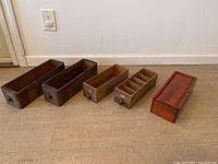 Full view of all five wooden storage boxes arranged on floor showing variety in size, shape and wood finish.