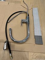 Full view of the chrome kitchen faucet laid flat with attached hoses and lever handle visible, placed on cardboard.