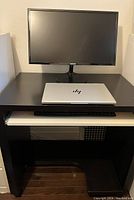 Chocolate brown computer desk with white pull-out keyboard shelf, shown with a monitor and laptop on top, against a wall on wooden floor.