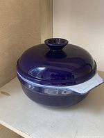 Cobalt blue round casserole with lid shown from side angle on shelf.