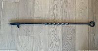 Full length photo of vintage iron fireplace poker on wood floor showing twisted design and hook end.
